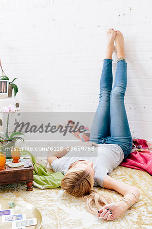 A young woman in jeans lyng on her back with her legs against the wall.