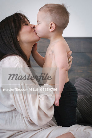 A heavily pregnant woman kissing her young son.