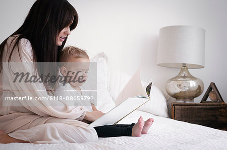 A heavily pregnant woman playing with her young son. Sitting on a bed, reading a story.