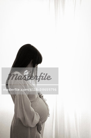 A heavily pregnant woman with her hands on her stomach seen in profile.
