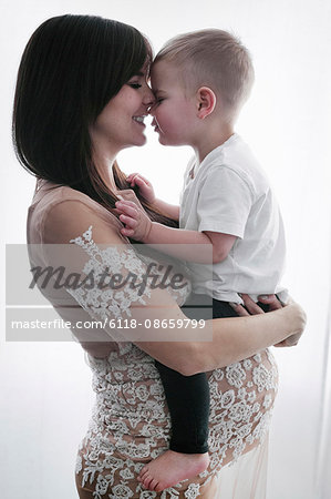 A pregnant woman holding her young son in her arms.