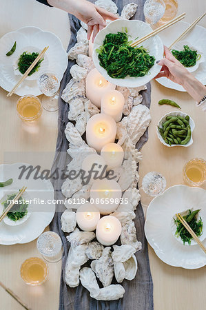 Overhead view of four people sharing a meal, plates of sushi and a table setting for a celebration meal.
