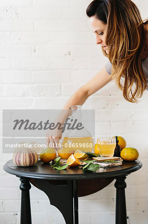 A woman arranging cut oranges on a table beside a tall jug of juice.