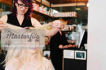 A hair stylist and a client, a young woman with long blonde hair, at a hair salon.