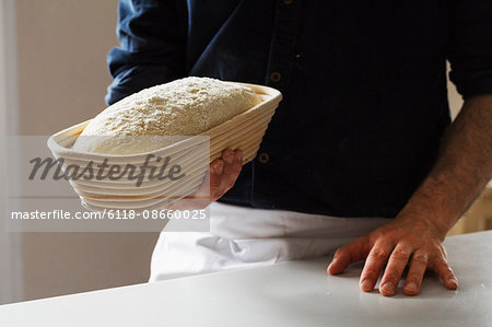 Close up of a baker holding a freshly baked loaf of white bread in a rattan proofing basket.