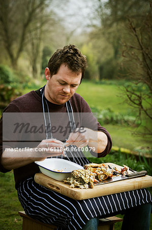 Chef sitting outdoors with a chopping board on his lap, preparing a crab.