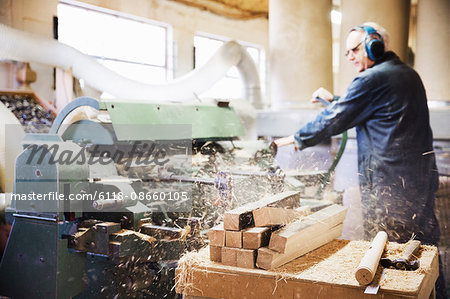 Man standing in a carpentry workshop, wearing hearing protectors, working at a woodworking machine.