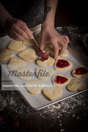 Valentine's Day baking, woman spreading raspberry jam on heart shaped biscuits.