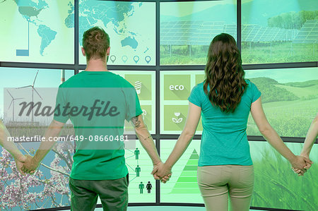 Four people standing, holding hands, in front of graphical screens, displaying environmental images
