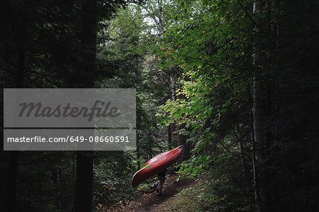 Mid adult woman carrying canoe through forest
