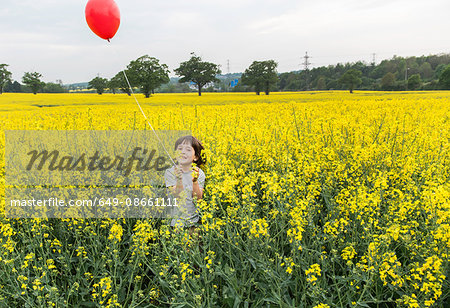 Portrait of boy standing in yellow flower field holding red balloon