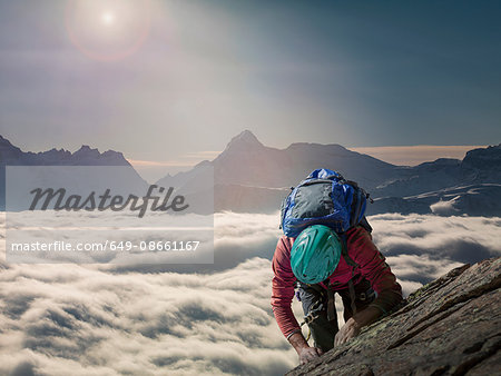 Climber on a rocky wall above a sea of fog in an alpine valley, Alps, Canton Wallis, Switzerland