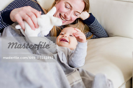 Baby girl and mother playing with toy rabbit on sofa