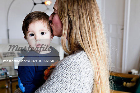 Mid adult woman carrying baby son and kissing his head