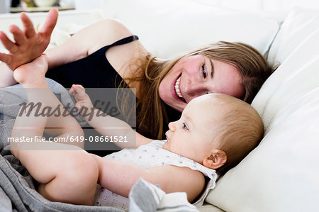 Mid adult woman playing with baby daughters bare feet on sofa