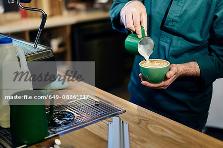 Cropped shot of male barista pouring milk into coffee cup in coffee shop