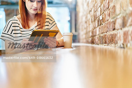 Young woman sitting at bench browsing digital tablet in coffee shop