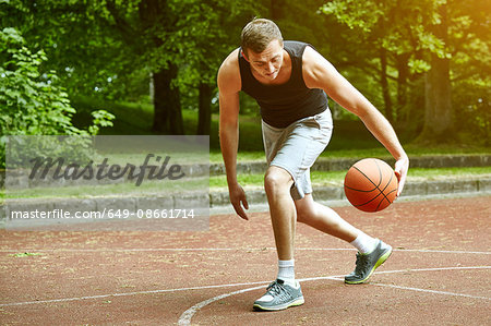 Young male basketball player running with ball on court