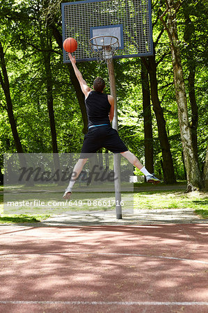 Rear view of young male basketball player jumping and throwing ball at hoop