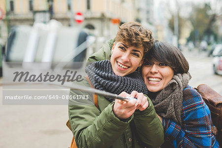 Two sisters, taking self portrait using selfie stick, outdoors