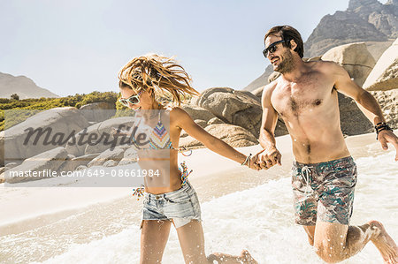 Couple wearing swimwear running on beach, Cape Town, South Africa