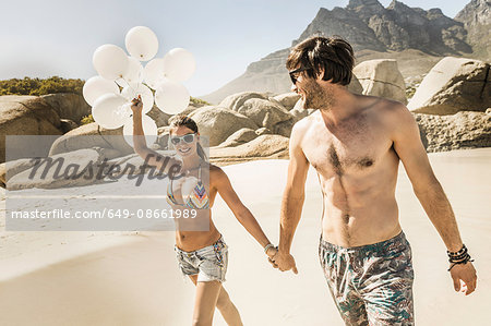 Couple holding bunch of balloons strolling on beach, Cape Town, South Africa