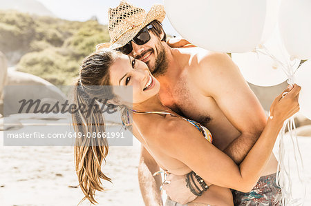 Portrait of couple holding bunch of balloons hugging on beach, Cape Town, South Africa