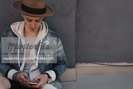 Young man leaning against wall, using smartphone