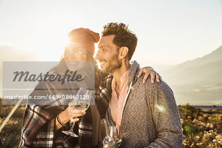 Couple in field holding wine glasses looking away