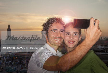 Young couple taking selfie in front of Jemaa el-Fnaa Square at sunset, Marrakesh, Morocco