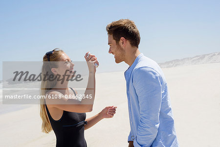 Woman spraying sunscreen on her husband face