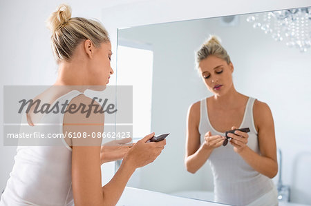 Beautiful young woman applying moisturizer on her face in bathroom