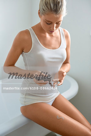 Beautiful young woman applying moisturizer in bathroom