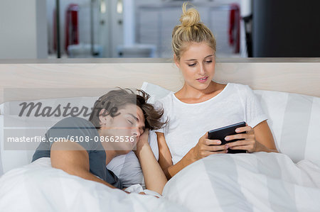 Young woman using a digital tablet with her boyfriend sleeping near her