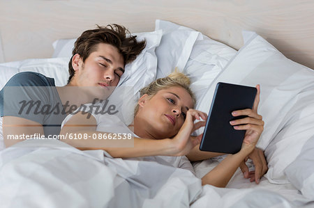 Young woman using a digital tablet with her boyfriend sleeping near her