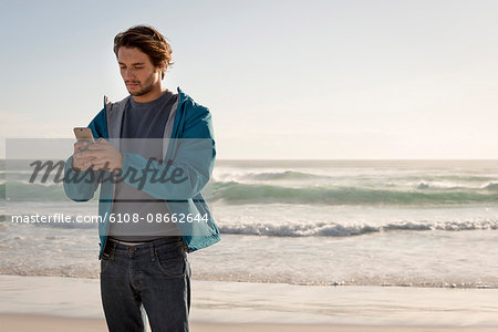 Happy young man using a mobile phone on beach