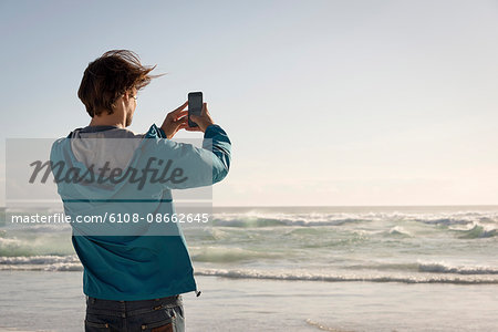 Happy young man taking picture with camera phone on beach