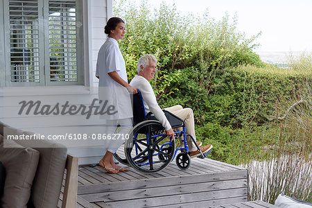 Female nurse assisting senior man in wheelchair on porch