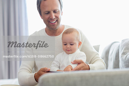 Happy father and his baby daughter playing with mobile phone on couch
