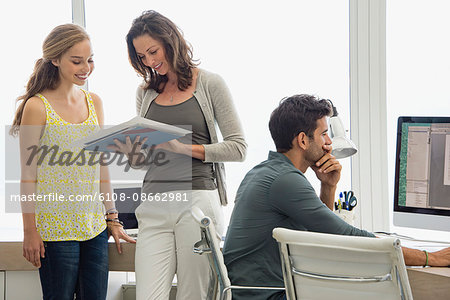 Businesswoman discussing file with her colleague with a man working on pc