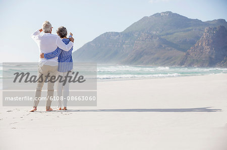 Rear view of a couple standing with arm around each other on the beach