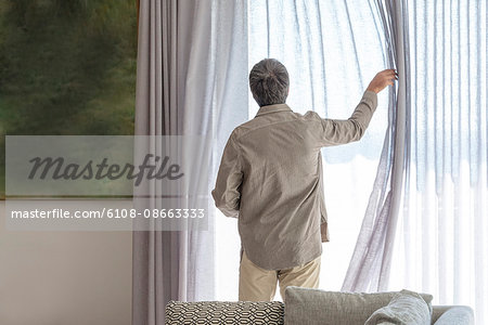 Rear view of a man holding curtain on window