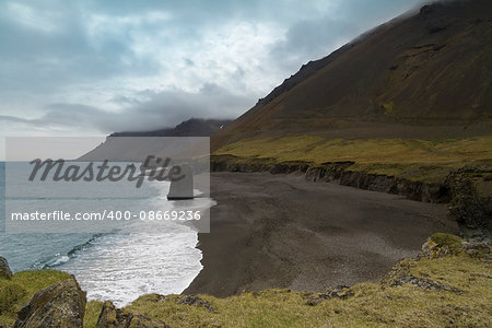 Horizontal view of an Icelandic beach with a huge rock formation in the middle