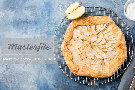 Apple galette, pie, tart with cinnamon on cooling rack on a blue stone background. Top view