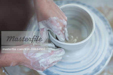 Close up of female potter's hands shaping clay bowl on pottery wheel in workshop