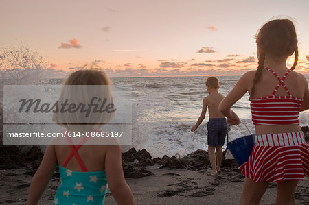 Boy and sisters watching splashing waves at sunrise, Blowing Rocks Preserve, Jupiter Island, Florida, USA