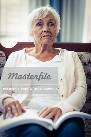 Pensive blind woman sitting on sofa with braille book on lap