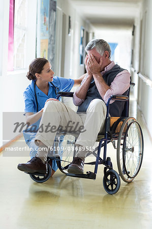 Female doctor consoling senior man in corridor at hospital