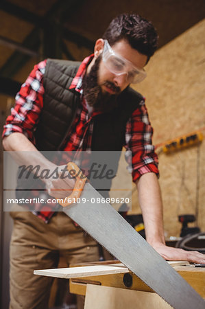 Carpenter sawing a plank of wood in carpentry