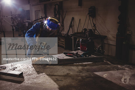 Welder cutting metal with grinder in workshop